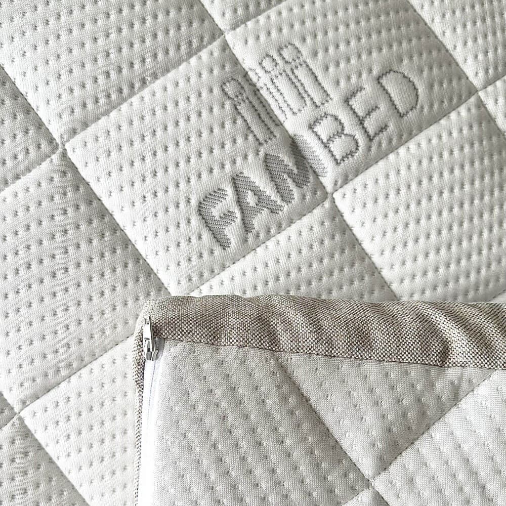 Primer plano de la funda blanca acolchada del sobrecolchón, con el logotipo de FAMBED integrado en el tejido