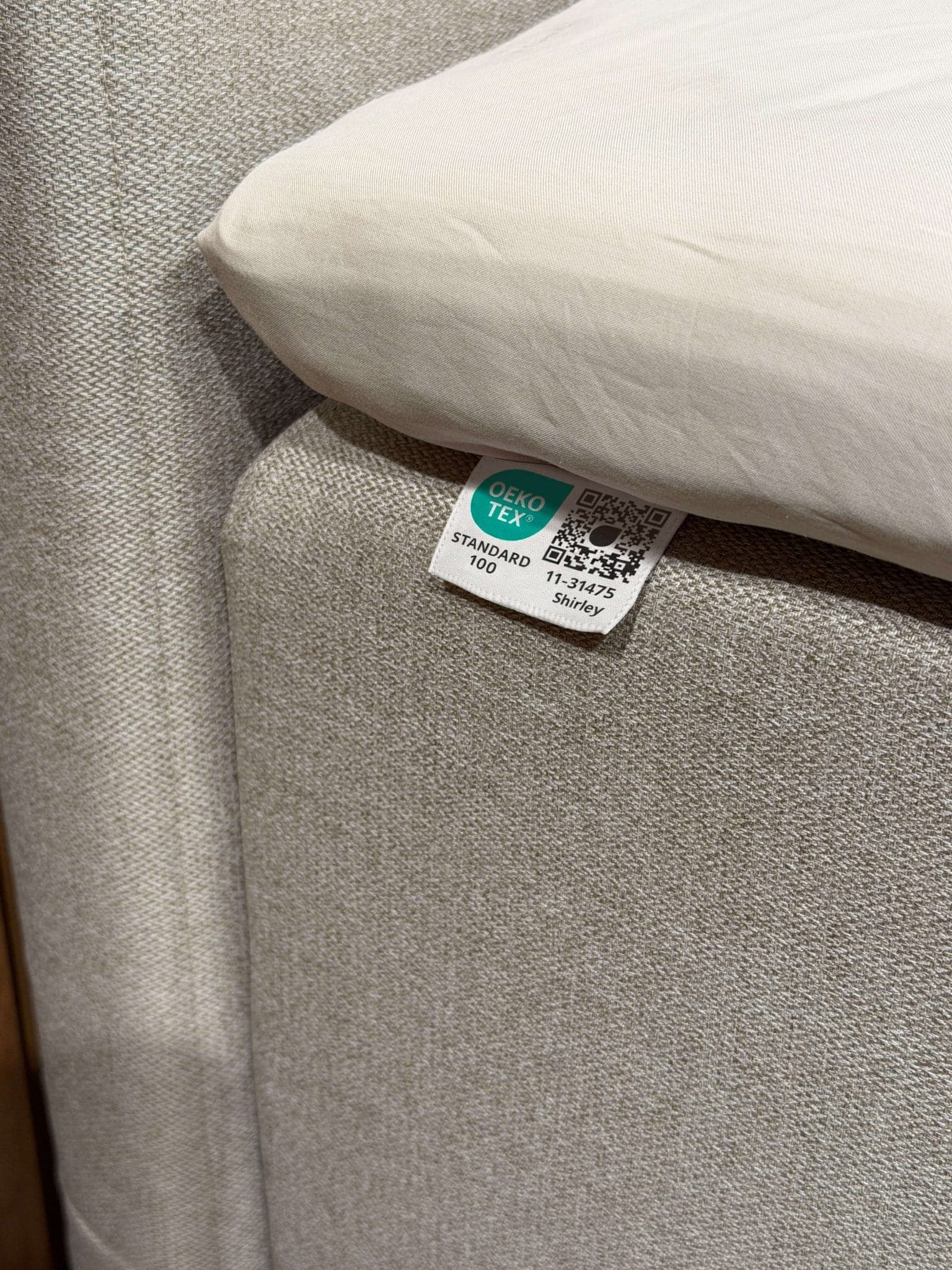 Etiqueta OEKO-TEX® STANDARD 100 cosida al tejido beige de la cama, debajo de la sábana