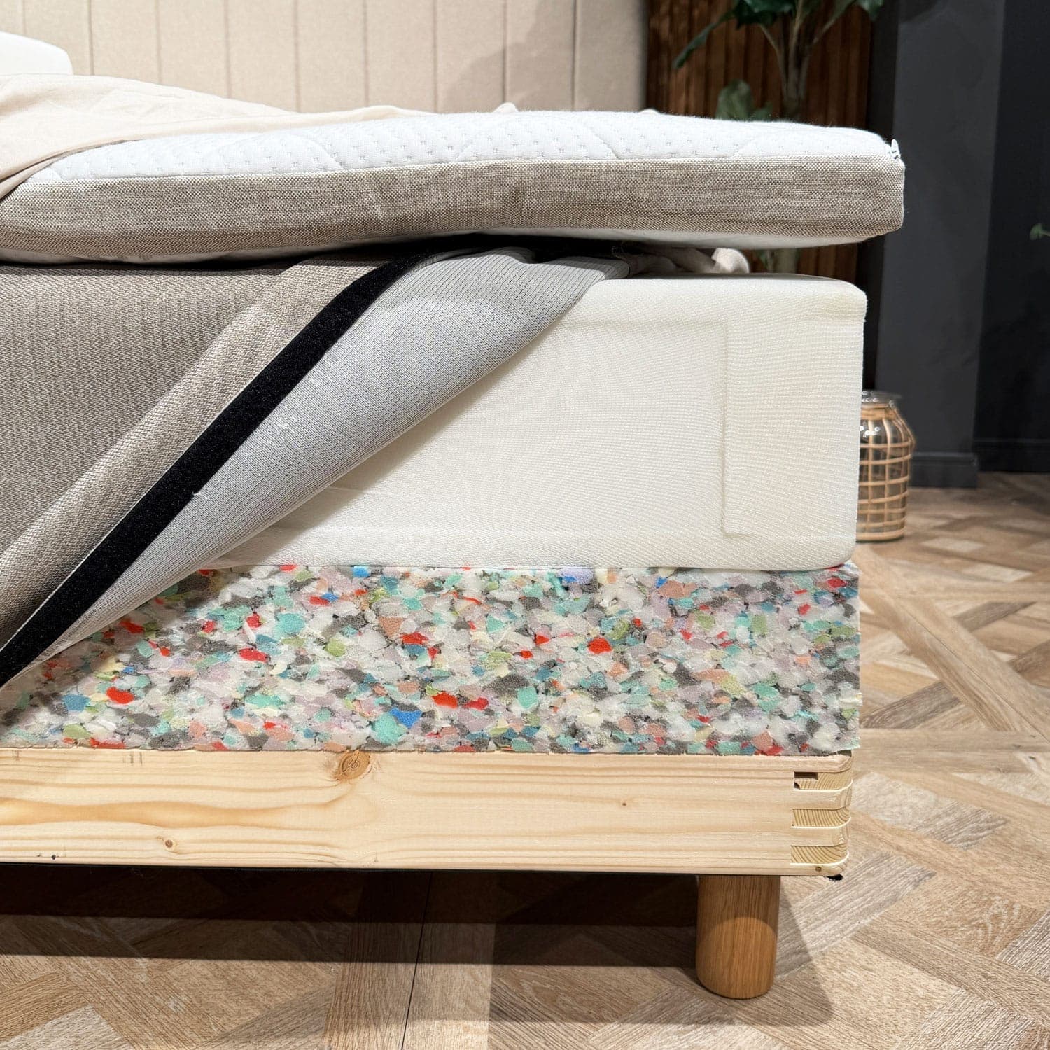 Capas de la cama abiertas en una esquina: sobrecolchón, colchón de muelles con la funda abierta y borde de espuma de la base sobre el bastidor de madera