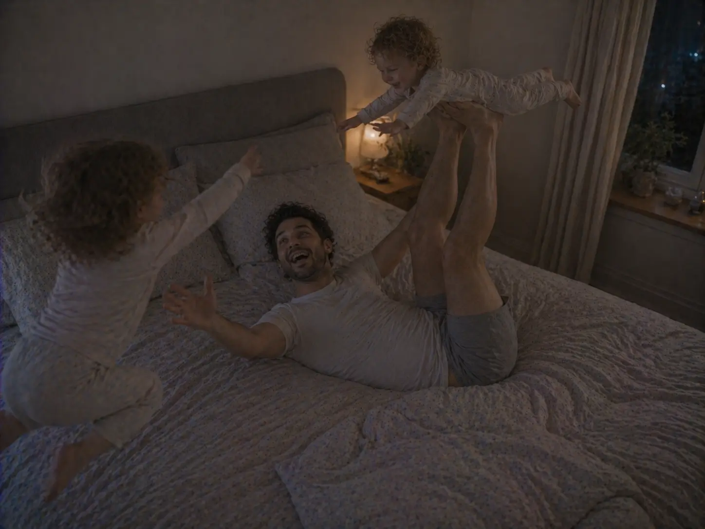 Un padre juega a hacer volar a uno de sus hijos sobre la cama mientras el otro salta a su lado