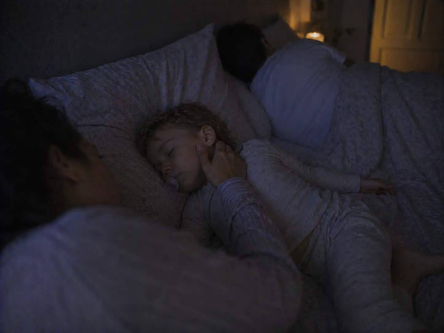 A mother gently touching her sleeping child's cheek in the family bed at night